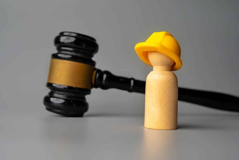 Una figura de madera con un casco amarillo junto a un martillo simboliza el apoyo jurídico a los trabajadores de la construcción accidentados en las obras de Brooklyn.
