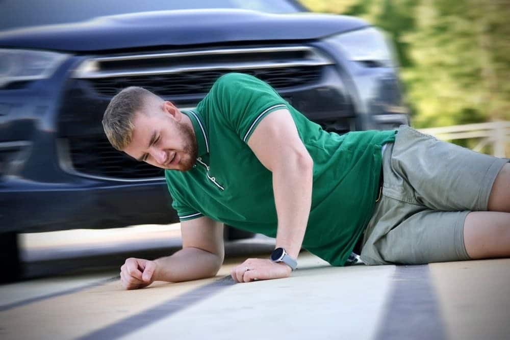 Un hombre con camisa verde tendido en el suelo tras ser atropellado por un coche, con el vehículo difuminado al fondo, poniendo de relieve la importancia de la seguridad de los peatones y sus derechos legales en Nueva York.