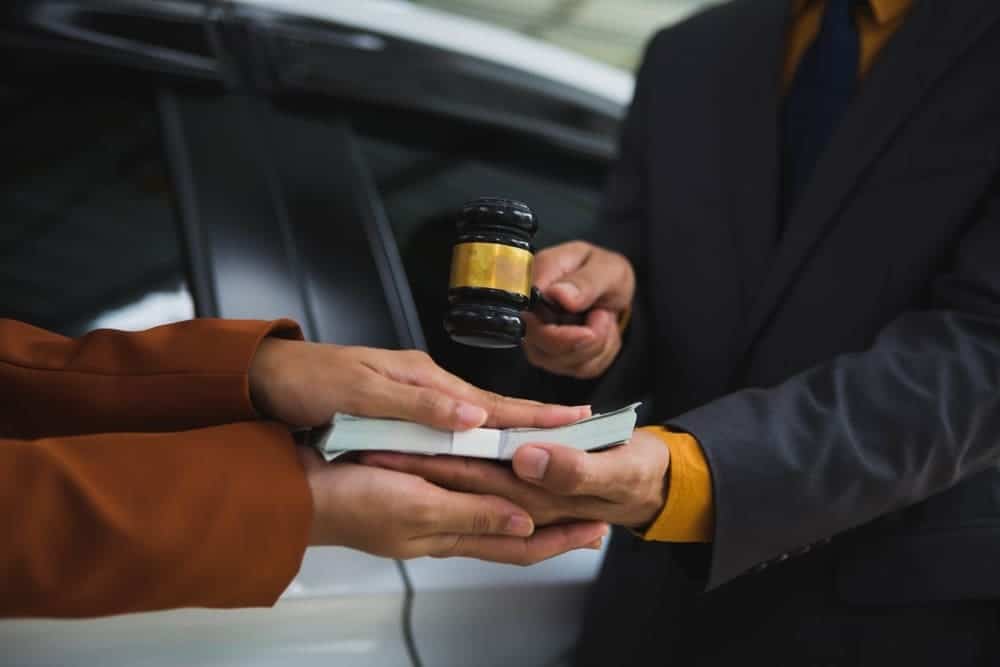 Un abogado de accidentes de coche en Nueva York sostiene un mazo mientras acepta el pago de un cliente cerca de un vehículo, símbolo de la representación legal y la indemnización por reclamaciones de accidentes de coche.