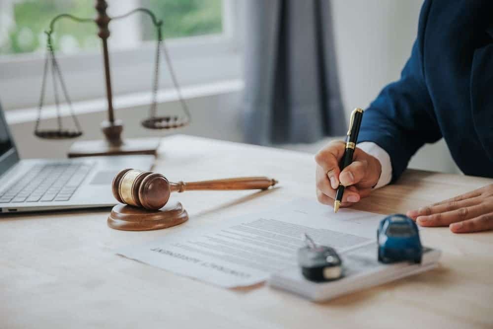 Attorney signing legal documents at a desk with a gavel, scales of justice, and car keys during a New York personal injury lawyer consultation.