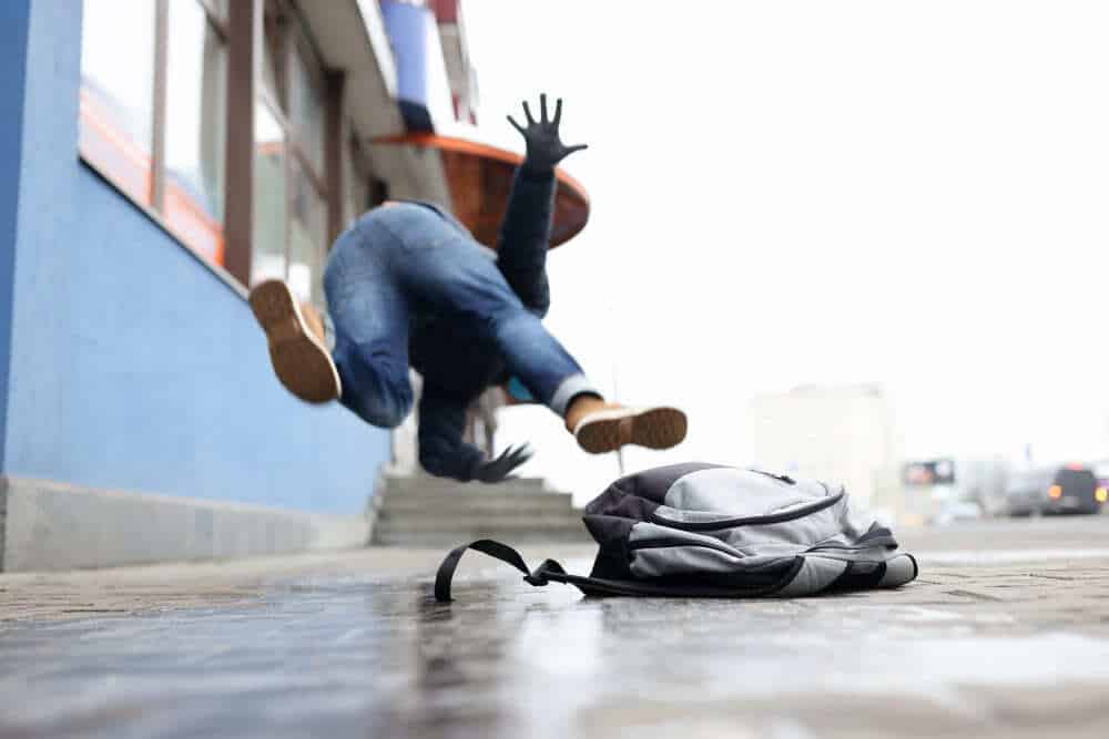 Person falling on a wet sidewalk near a building entrance, illustrating a New York slip-and-fall or sidewalk accident injury claim.
